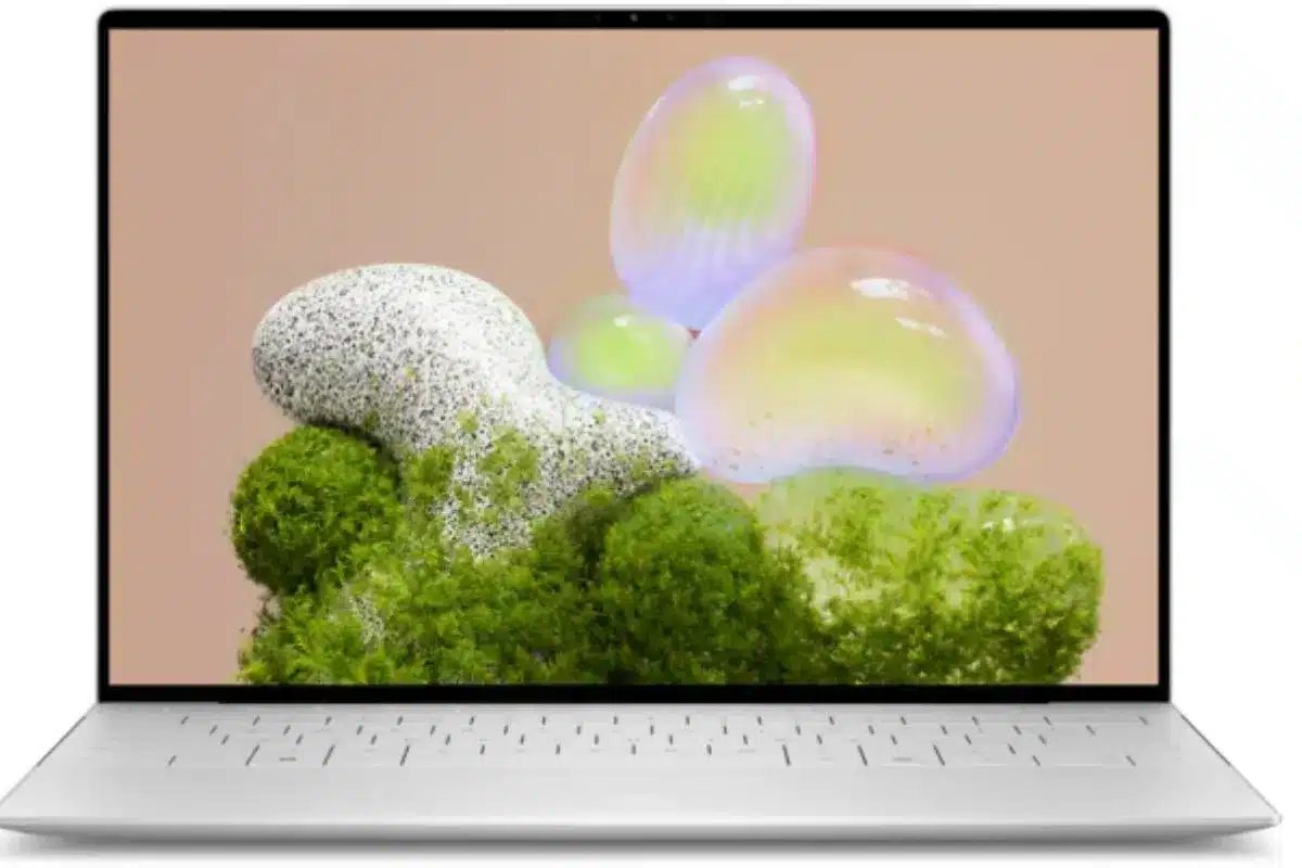 Dell XPS 13 aberto, visto de frente, com acabamento prateado e tela exibindo formas abstratas coloridas sobre fundo bege.
